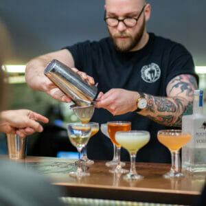 Man wearing a black branded t shirt making cocktails during cocktail masterclass